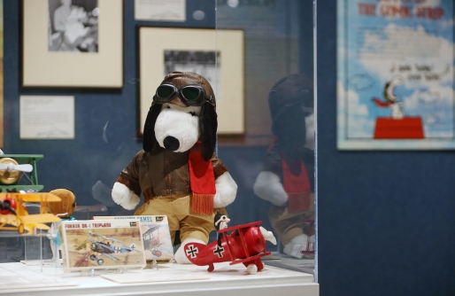 Plush Snoopy in Aviator Jacket, Hat and Goggles with small model airplanes in case, artwork and poster images in background