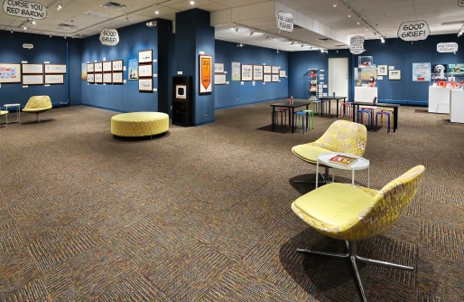 Blue Walls hung with Snoopy Cartoons in background, yellow modern chairs in foreground, activity tables and display cases