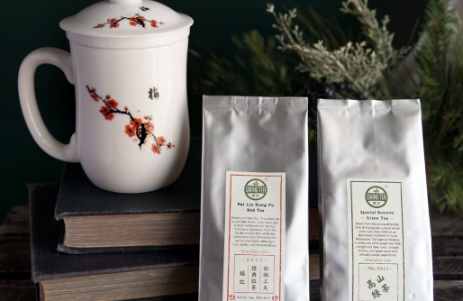 White Tea Cup with orange cherry blossom sitting on books.  Two sliver bags of Shang Tea, sample size.