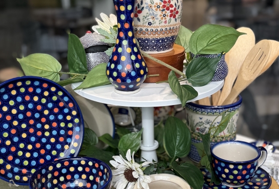 Polish Potter ItemsTop to Bottom: Floral Lidded Jar, Polk Dot Blue Vase, Plate, Bowl, Cup and Saucer, Floral Patern Utensil Holder with wooden spoons, Pitcher, Mug and Covered butter dish in floral and fruit patterns.