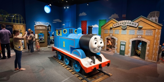Blue Thomas engine in front of other structures with woman taking pictures